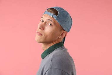 Pembe arka planda şık bir beyzbol şapkası takan genç adam.