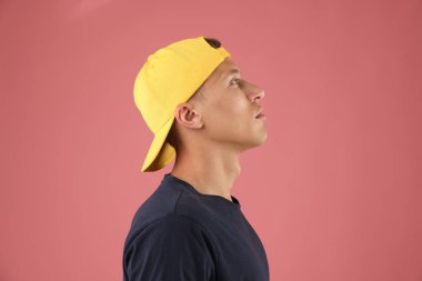 Pembe arka planda şık bir beyzbol şapkası takan genç adam.