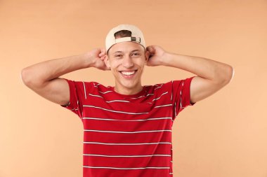 Beyzbol şapkalı genç adam bej arka planda.