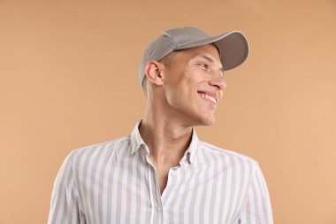 Beyzbol şapkalı genç adam bej arka planda.