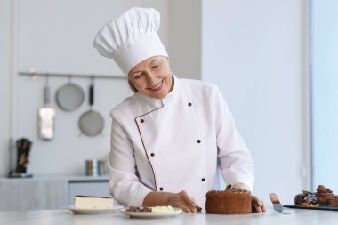 Gülümseyen pasta şefi mutfaktaki tatlılarla masada.