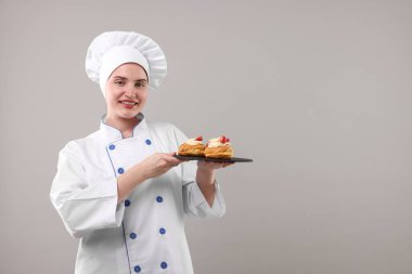 Üniformalı şekerci açık gri arka planda lezzetli profiteroller tutuyor, mesaj için yer var.