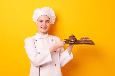 Üniformalı şekerlemecinin elinde turuncu arka planda lezzetli çikolatalı tatlılar var.