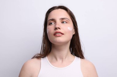 Yüzünde açık gri arka planda cilt ürünü olan güzel bir kadın, yakın plan.