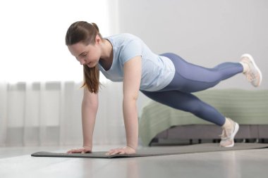 Spor kıyafetli bir kadın evde kalas egzersizi yapıyor.