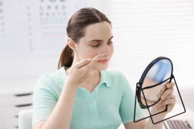 Göz doktorunun ofisinde aynanın yanında lens takan genç bir kadın.