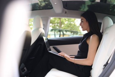 Modern arabada dizüstü bilgisayar kullanan bir kadın. Dışarıdan görünüyor.