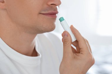 Genç adam evde dudaklarına merhem sürüyor, yakın plan.