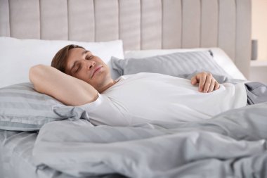 Evdeki yumuşak yatakla yatakta uyuyan genç adam.