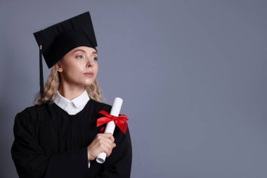 Mezuniyetten sonra gri arka planda diplomalı bir öğrenci. Metin için boşluk