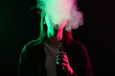 Siyah arka planda neon ışıkları altında elektronik sigara içen kadın