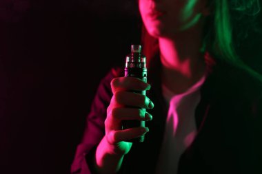 Siyah arka planda neon ışıklarda elektronik sigara içen bir kadın, yakın plan. Metin için boşluk