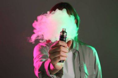 Gri arkaplandaki neon ışıklarda elektronik sigara içen kadın, seçici odaklanma