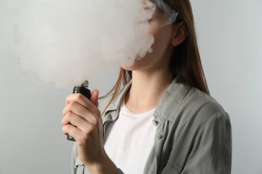 Açık gri arkaplanda elektronik sigara içen kadın