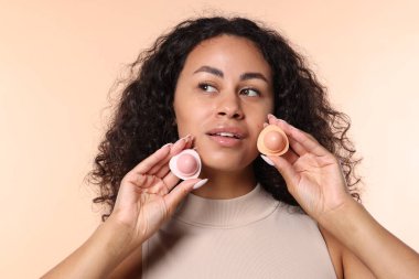 Bej arka planda dudak merhemi dolu kaplarla gülümseyen kadın.