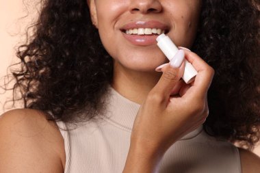 Gülümseyen kadın dudaklarına krem sürüyor. Bej arka planda, yakın plan.