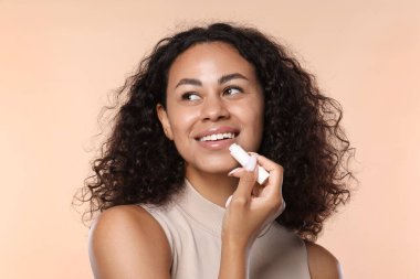 Gülümseyen kadın bej arka planda dudaklarına merhem sürüyor.