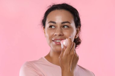 Gülümseyen kadın pembe arka planda dudaklarına merhem sürüyor.