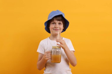 Panama şapkalı, turuncu arka planda meyve suyu kavanozu olan şirin bir çocuk. Tazeleyici içecek.