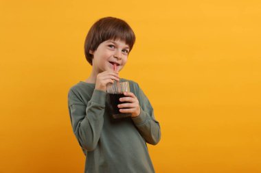 Tatlı küçük çocuk turuncu arka planda ferahlatıcı soda içiyor.