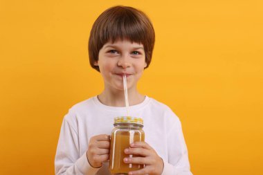 Turuncu arka planda meyve suyu içen tatlı bir çocuk. Tazeleyici içecek.