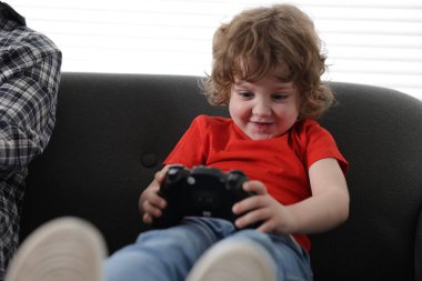 Küçük çocuk ve babası evde oyun kontrolörüyle oynuyorlar.