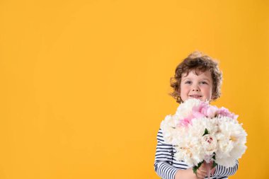 Sarı arka planda bir buket güzel şakayığı olan sevimli küçük bir çocuk. Metin için boşluk