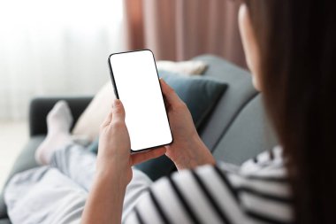 Evdeki koltukta modern akıllı telefon kullanan bir kadın.