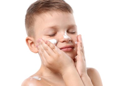 Küçük çocuk beyaz arka planda cildine güneş kremi sürüyor.