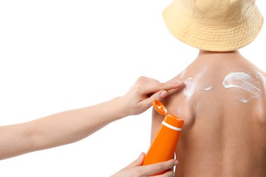 Anne beyaz arka planda oğlunun cildine güneş kremi sürüyor.