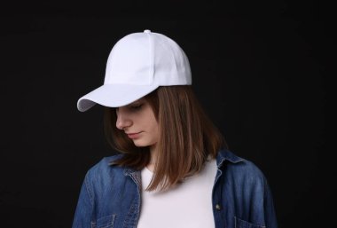 Siyah arka planda şık beyaz beysbol şapkası giyen genç bir kadın.