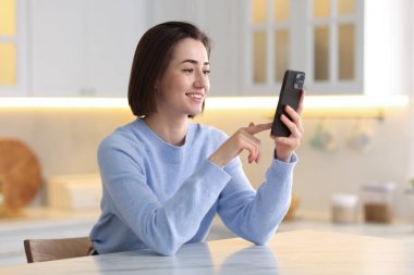 Mutfaktaki masada modern akıllı telefon kullanan bir kadın.