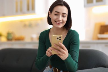 Evdeki koltukta modern akıllı telefon kullanan bir kadın.