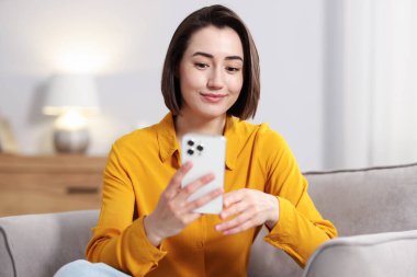 Evdeki koltukta modern akıllı telefon kullanan bir kadın.