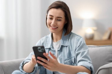 Evdeki koltukta modern akıllı telefon kullanan bir kadın.