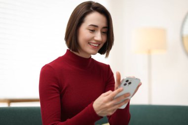 Evdeki koltukta modern akıllı telefon kullanan bir kadın.