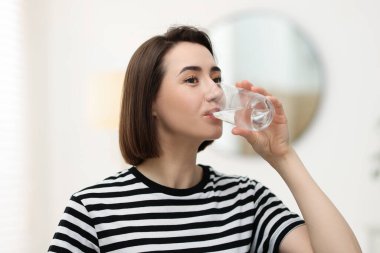 Genç bir kadın evde camdan su içiyor.
