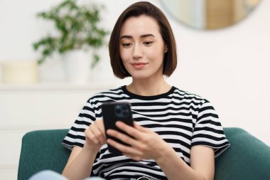 Evdeki koltukta modern akıllı telefon kullanan bir kadın.