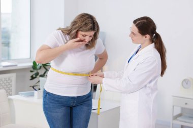 Kilo kaybı. Klinikte aşırı kilolu bir kadının belini bantla ölçen beslenme uzmanı.