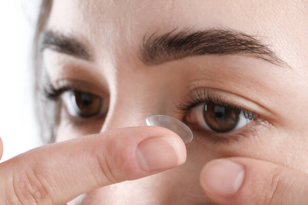 Woman putting in contact lens on white background, closeup