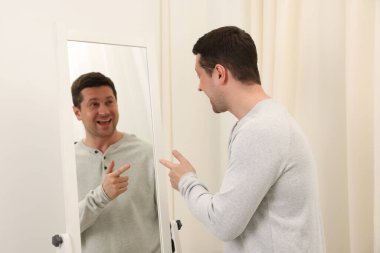 Yakışıklı adam aynada kendine bakıyor.