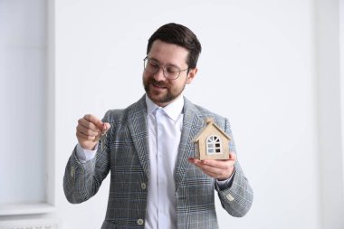 Emlakçının elinde anahtarlık ve ev modeli var.