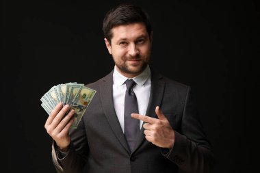 Açgözlü bankacı siyah arka planda dolar banknotlarını işaret ediyor