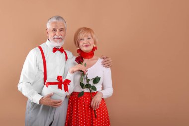 Hediye kutusu ve açık kahverengi arka planda gül olan sevimli son sınıf çifti, mesaj için yer var.