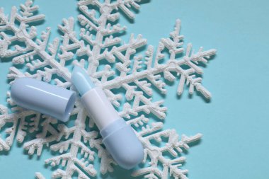 Nemlendirici dudak kremi ve açık mavi arka planda Noel dekoru, düz yatış. Kış bakımı