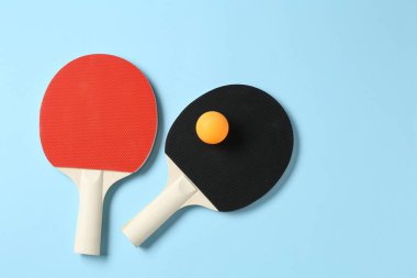 Masa tenisi raketleri ve top açık mavi arka planda, düz yerde. Metin için boşluk