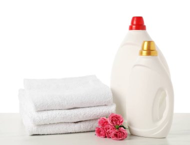 Kumaş yumuşatıcı şişeler, beyaz arkaplana karşı mermer masaya yığılmış havlular ve çiçekler.