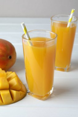 Bardakta lezzetli mango suyu ve beyaz ahşap masada taze meyve, yakın plan.