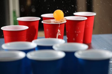Bira pong oyunu. İçkili plastik bardaklar ve masada top, yakın plan.