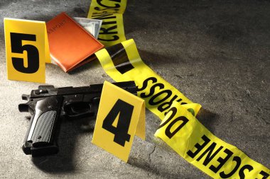 Adli tıp uzmanı. Sarı olay yeri bandı, silah, pasaport ve para gri masada, yakın plan. Metin için boşluk
